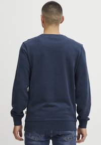 Felpa blu navy con maniche lunghe, polsini e orlo a coste, colletto rotondo e una texture liscia. Presenta un sottile dettaglio di cucitura sul retro.