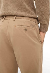 Beige broeken met een achterzak met knoopsluiting, gemaakt van zachte katoenstof, met een gestructureerd oppervlak en een verstelbare tailleband.