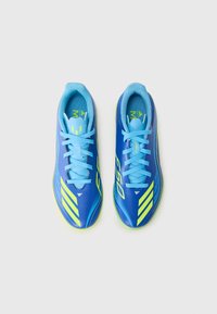 Botas de fútbol sintéticas azules con acentos amarillos, cinco rayas a cada lado y un acabado texturizado. Los cordones coinciden con el color del calzado.