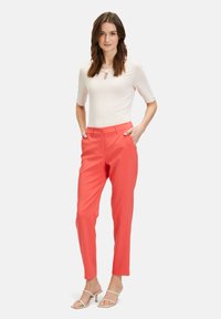 Korallowe spodnie w kant o dopasowanym kroju, z paskami, przednimi kieszeniami i zapięciem na guzik. Połączone z jasnym dopasowanym topem.