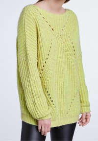 Pull en maille de couleur jaune-vert vif, avec des manches surdimensionnées, des motifs à mailles ajourées et des poignets et ourlet côtelés.