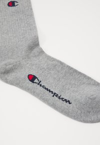 Grau melierte Baumwollsocke mit einem roten und blauen Logo, geripptem Muster und aufgesticktem "Champion" in Marineblau an der Seite.