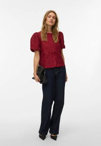 Rød tekstureret bluse med puffede ærmer, kombineret med mørkevidde cowboybukser og sort clutch. Højhælede spidse sko fuldender looket.