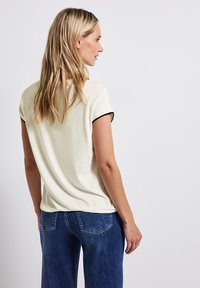 Krämfärgad t-skjorta med kort ärm och svart kant, mjukt tyg, avslappnad passform. Matchas med blå denimjeans med bakfickor och blekt mönster.