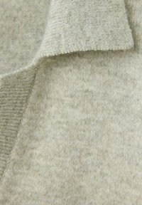 Gros plan sur un tissu tricoté beige clair avec des bords repliés, montrant une texture douce et un motif fin de tricot.