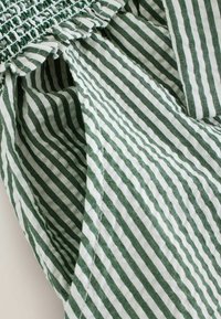 Tissu rayé verticalement vert et blanc avec couture élastique froncée et surpiqûres visibles.