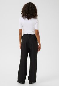 Zwarte wijde broek met een elastische tailleband, gecombineerd met een strakke witte top. Soepele textuur, minimalistisch ontwerp, geschikt voor casual wear.