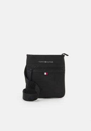 Sort Tommy Hilfiger crossbody taske med lynlåslomme foran, logotekst, flagdetalje og justerbar rem på hvid baggrund.
