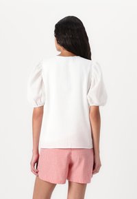 Blouse blanche texturée avec des manches bouffantes, associée à un short rayé rouge et blanc. Vue de dos, tissu lisse, design décontracté.