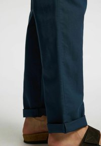 Mörkblå bomullsbyxor med uppvikta fållar, med en mjuk textur och skräddarsydd passform, i kombination med mörka sandaler.