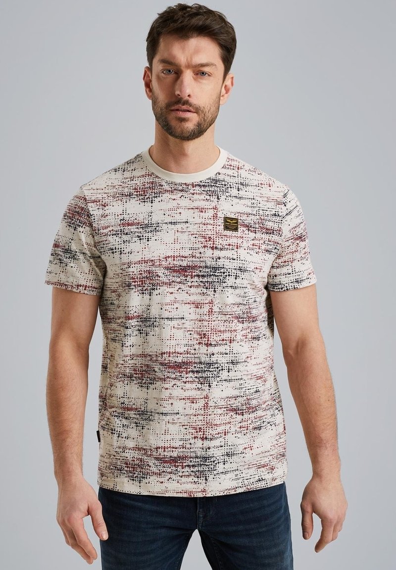 T-shirt i creme med et geometrisk mønster i rød og sort. Har en rund halsudskæring og et lille mærke på brystet.