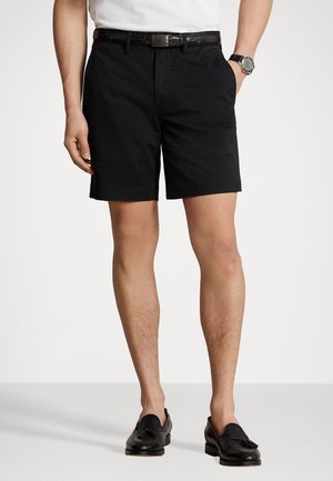 Zwarte katoenen shorts met zijzakken, met een vlakke voorkant en opgerolde hems, gecombineerd met zwarte loafers en een donkere leren riem.