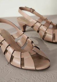 Vaaleanpunaiset nahkaiset slingback-sandaalit, joissa on leikkauksen muotoilu, avonainen kärki ja kohtuullinen korko. Varusteena on solki, jonka avulla saa säädettyä istuvuutta.