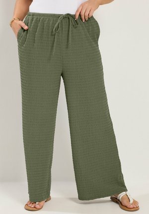 Pantaloni larghi di colore verde oliva con texture, con elastico in vita e coulisse, indossati con sandali bianchi e top bianco.