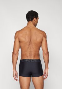 Zwarte boxershorts met een gladde textuur, voorzien van een brede tailleband met het woord "RAIDER" erop gedrukt. Het ontwerp is nauwsluitend.