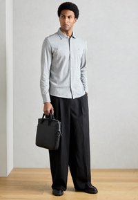 Camisa cinzenta de manga comprida com botões e gola, calças pretas de perna larga e uma mala de pele preta com pegas superiores. Design simples e limpo.