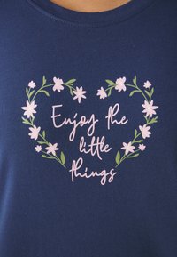 Navy blue cotton t-shirt featuring a floral heart design with light pink flowers and the text "Enjoy the little things" in playful font.