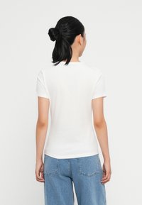 Tricou alb cu mânecă scurtă, de tip crew neck, cu un design ajustat și o textură moale, purtat cu blugi lejeri de culoare bleu deschis.
