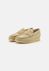 Beige suède loafers med rund tå, sydde detaljer og en lav kile såle. Glatt tekstur med et enkelt design.