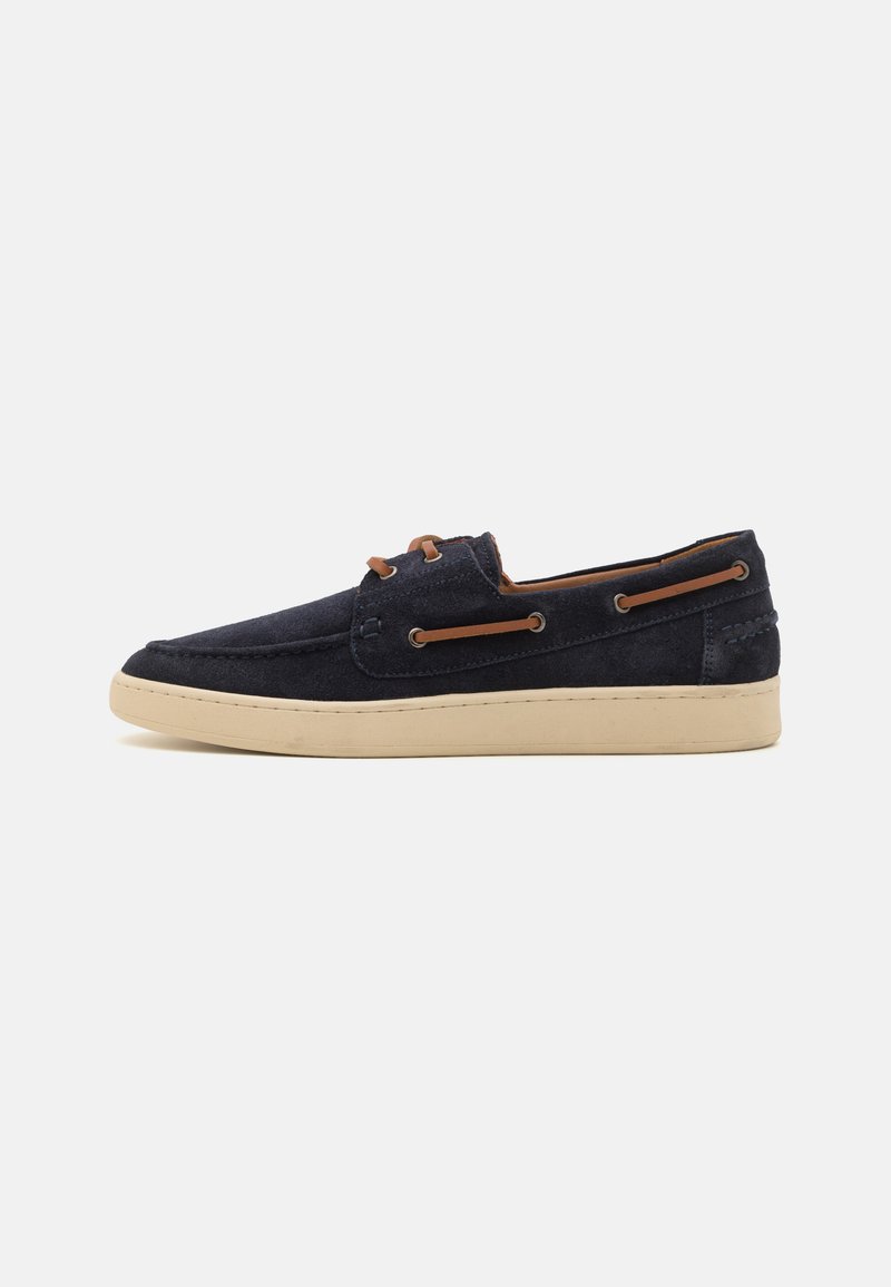 Navy suede boat shoe with a round toe, cream rubber sole, and leather lacing accents. Features a stitched pattern on the upper.