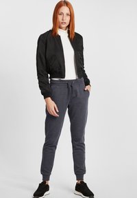 Svart bomberjacka med frontdragkedja, ribbade ärmslut och sidofickor. Matchad med marinblå joggingbyxor med justerbar dragsko i midjan. Svarta sneakers.