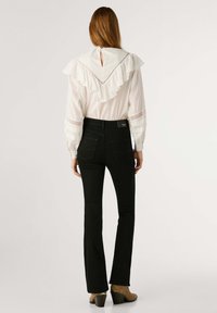 Blusa blanca con cuello volado, detalles de encaje en las mangas, combinada con jeans negros acampanados y zapatos de tacón. Diseño minimalista.