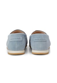 Light blue suede slip-on shoes with rounded back, white rubber sole, and embossed branding on the heel. Smooth texture, casual design.