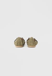 Zapatos de ante verde oliva con punta puntiaguda y diseño recortado, con suela de cuero natural. Sin herrajes ni detalles visibles.