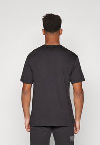 T-shirt noir à manches courtes en coton doux avec une coupe décontractée. Il présente un col rond et un logo discret dans le bas du dos.