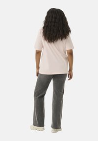 T-shirt en coton rose, à manches courtes, coupe ample, associé à un pantalon large gris. Le modèle est debout, montrant la vue arrière. Cheveux texturés.
