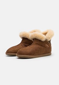 Brown suede slippers with a fluffy beige faux fur collar and a patterned fabric accent. Soft texture and rounded toe design.