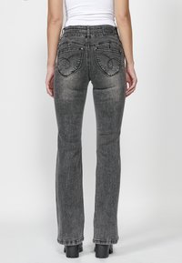 Vaqueros de mezclilla gris de corte acampanado con detalles en los bolsillos, que cuentan con bolsillos traseros bordados, una cintura alta y un acabado texturizado.