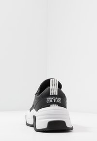 Black and white Versace Jeans Couture sneaker shown from the back, featuring a thick sole and branded heel tab with stitching details.