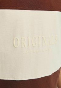 Ruda ir kreminė trumpo rankovėmis marškiniai su siuvinėtu "ORIGINALS" logotipu ir "JACK&JONES" po juo; sklandžios medvilnės audinio tekstūra.