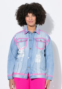 Veste en denim bleu clair, avec des coutures roses et des détails usés. Comprend des boutons argentés et un texte imprimé blanc à l'avant.