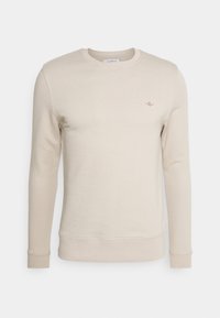 Sudadera beige de manga larga, con cuello redondo y un pequeño logo bordado. Confeccionada en un tejido suave, con puños y dobladillo ribeteados.