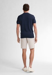 Maglietta a maniche corte in maglia blu abbinata a pantaloni corti a righe chiare, completata da sneaker beige. Outfit estivo semplice e informale.