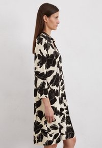 Motivo a foglie nere su un vestito bianco sporco con colletto, dotato di maniche tre quarti e un fit morbido, che arriva a metà coscia.