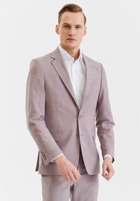 Jasnofioletowy garnitur o dopasowanym kroju z klapami w kształcie notcha, jednozapięciowy, na dwa guziki, z kieszeniami po bokach. Noszony na białej koszuli.