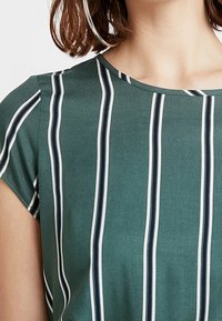 Grön topp med korta ärmar, rund halsringning och vertikala ränder i vitt och marinblått. Mjuk textur, avslappnad design.
