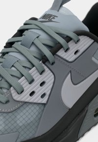 Nike sneaker featuring a light gray upper with mesh accents, rubber sole, textured overlays, and tonal laces.