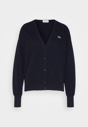 Cardigan lavorato a maglia blu navy con scollo a V, chiusura con bottoni, polsini e orlo a coste, con un piccolo logo verde a forma di coccodrillo sul lato sinistro del petto.