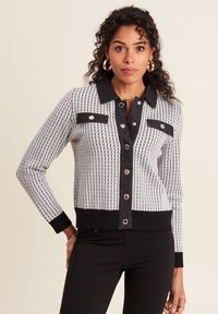 Cardigan à motifs noir et blanc avec fermeture à boutons, col sombre et accents de poches, poignets et ourlet côtelés, design ajusté.