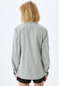 Camisa gris de manga larga con una textura sutil, puños abotonados y un dobladillo ligeramente curvado. Presenta un cuello clásico y un corte relajado.