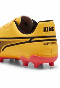 Geltonos futbolo bateliai su lygiu sintetiniu viršumi, juodais akcentais ir raudonu gradientiniu padu. Turintys tekstą "KING" ir "FOREVER.FASTER."