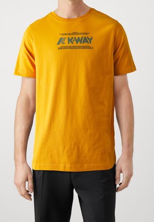 Lyhythihainen keltainen puuvillainen t-paita, jossa on pyöreä kaula-aukko ja tummanvihreä graafinen logo etupuolella. Sileä pinta, rento istuvuus.