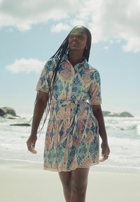 Robe à motif floral avec des manches courtes, col à boutons, ceinture nouée, en bleu, rose et crème, avec une dentelle au bas.