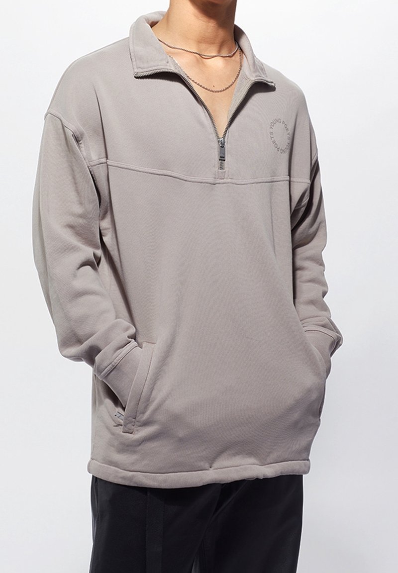 Světlounce šedý pulovr na čtvrtý zip z měkké látky, s vysokým límcem, žebrovanými manžetami a dvěma bočními kapsami. Jemný detail loga na hrudi.