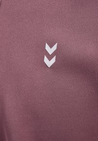 Gros plan sur un tissu mauve texturé avec deux flèches blanches en chevrons pointant vers le bas, centrées sur la surface.