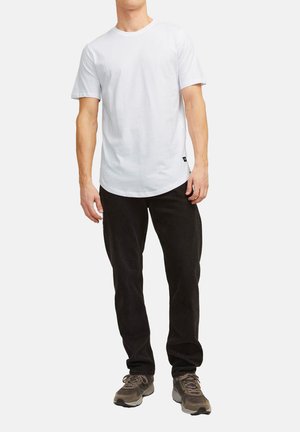 Weißes Baumwoll-T-Shirt mit kurzen Ärmeln und Rundhalsausschnitt, kombiniert mit schwarzen Cordhosen und grauen Turnschuhen. Einfacher, lockerer Schnitt.